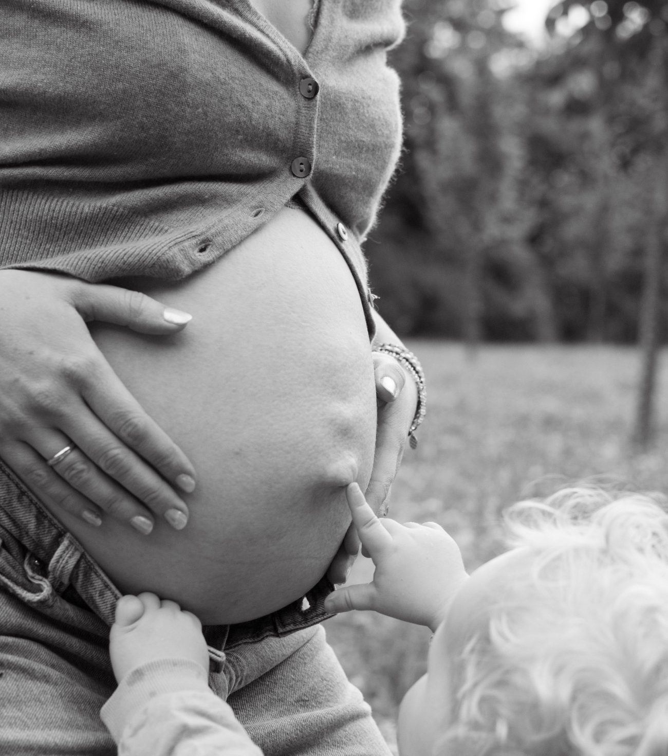 Schwarz-weiß: Ein Kleinkind tippt mit dem Finger auf den Babybauch der Mama