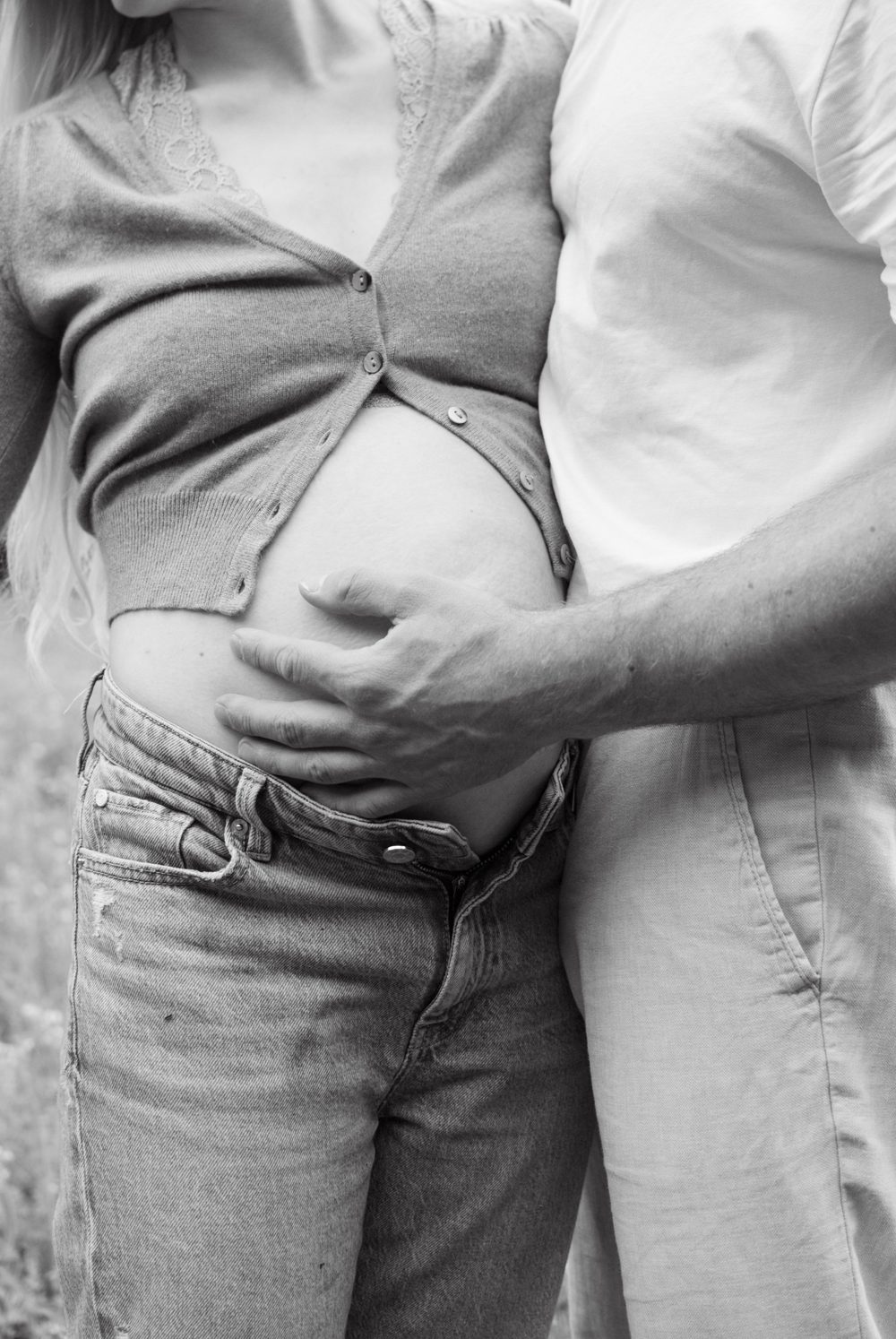 Schwarz-weiß: Die Hand des werdenden Vaters liegt auf dem nackten Babybauch