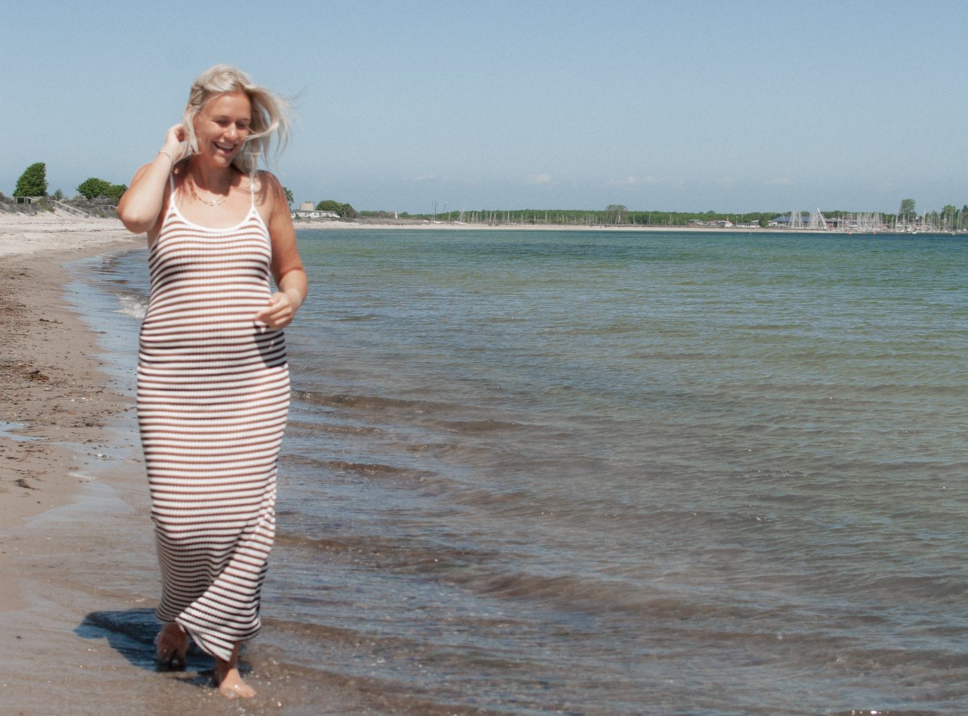 Die Schwangere läuft lachend barfuß durch das flache Wasser am Strand