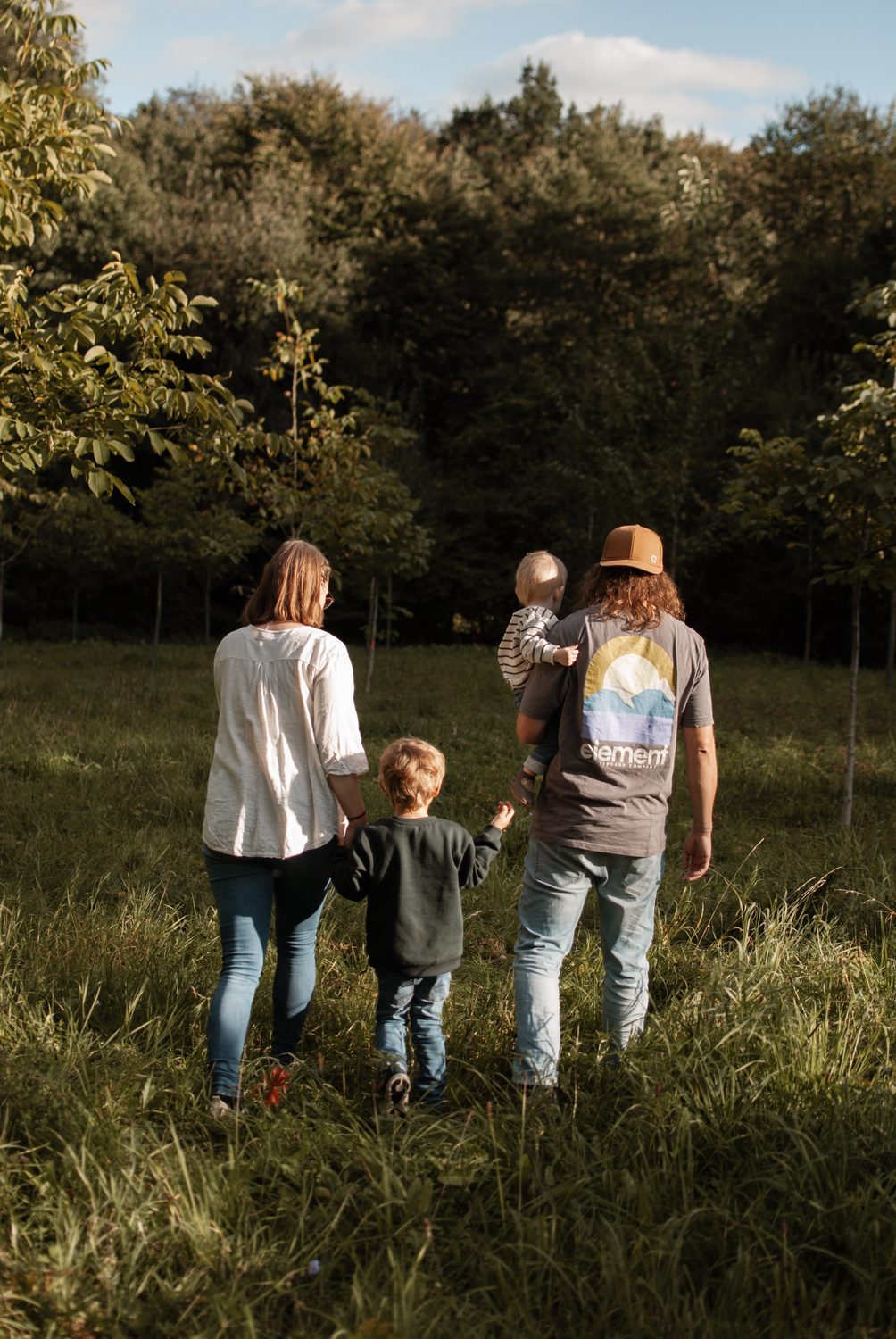 Die Familie geht von hinten gesehen gemeinsam über die Wiese auf den Waldrand zu